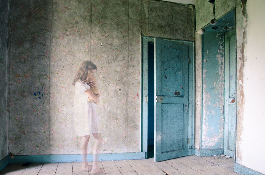 Kind im  Nachthemd, umklammert ängstlich ein Stofftier, steht vor einer hellblauen halbgeöffneten Tür, düstere Atmosphäre